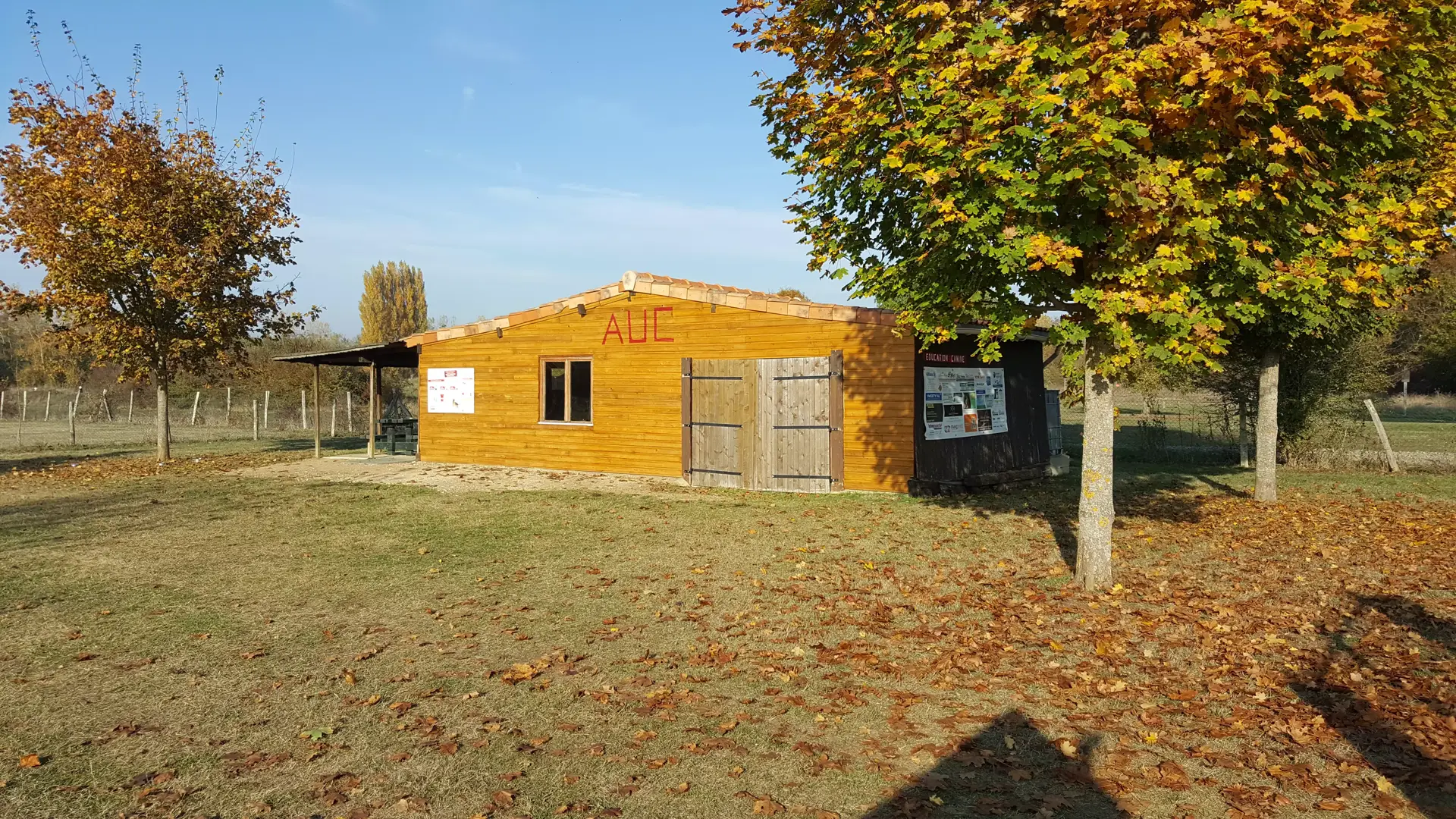 Le chalet du club, en bois clair, au milieu du terrain à l'automne